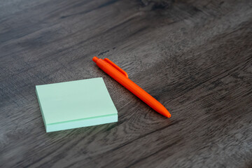 Blank green sticky note pad and orange pen on dark wooden desk background © Mihail