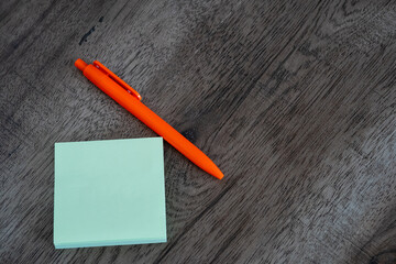 Blank green sticky note pad and orange pen on dark wooden desk background © Mihail