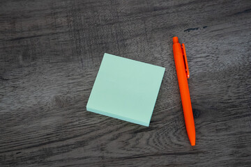 Blank green sticky note pad and orange pen on dark wooden desk background © Mihail