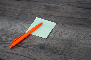 Blank green sticky note pad and orange pen on dark wooden desk background © Mihail