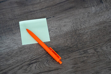 Blank green sticky note pad and orange pen on dark wooden desk background © Mihail