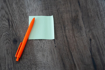 Blank green sticky note pad and orange pen on dark wooden desk background © Mihail