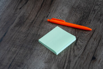 Blank green sticky note pad and orange pen on dark wooden desk background © Mihail