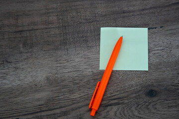 Blank green sticky note pad and orange pen on dark wooden desk background © Mihail