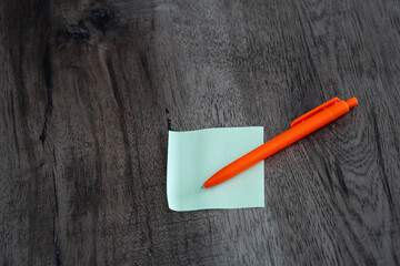 Blank green sticky note pad and orange pen on dark wooden desk background © Mihail