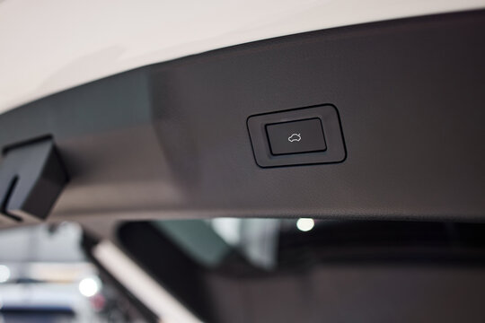 Detailed close view of vehicle interior roof control button beside rear hatch opening, set in headliner with soft studio light, shallow focus, clean modern trim
