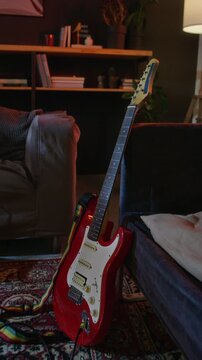 Vertical shot of red electric guitar leaning against sofa in home music studio. Footage is ideal for music school advertisements, hobby promotions, or creative lifestyle marketing campaigns