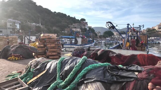 Large piles of colorful fishing nets and wooden crates on a harbor dock a low