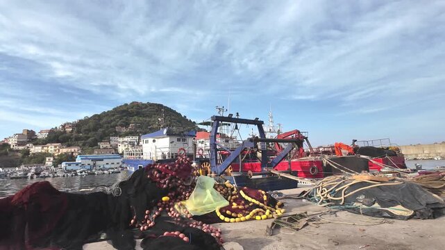 Blue and red fishing trawlers docked at harbor with piled fishing nets painted
