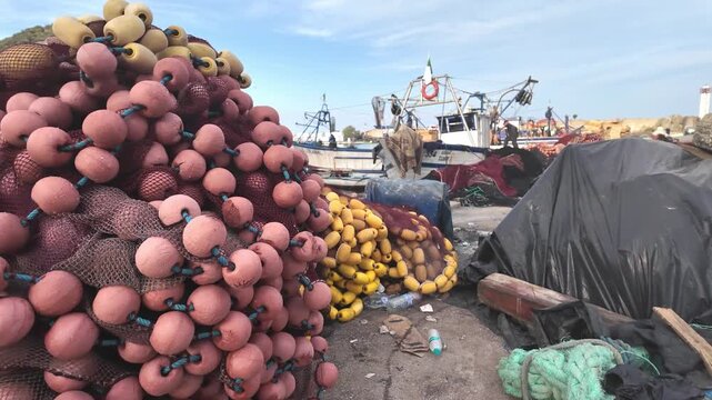 Fishing nets and colorful floats piled up on the dock at a coastal harbor