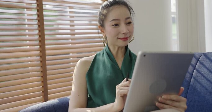 Asian business woman with attractive smile use tablet on coach, Portrait beauty girl relax living room. Technology people connection digital online marketing e-commerce 