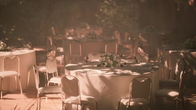 Tables are arranged under soft lighting in a serene outdoor venue. Floral centerpieces adorn each table, creating a charming ambiance for a gathering or celebration.