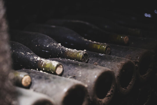 Dust‑covered wine bottles lie in rows inside a Beaune cellar in Burgundy, France, showing years of aging and tradition.
