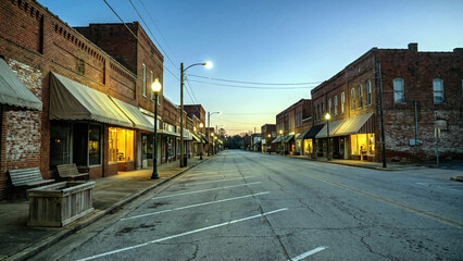 Fototapeta premium Quiet small town main street at dusk with warm lit shop windows