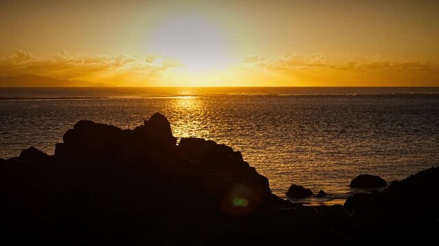 Aerial video along a tropical beach at dawn with golden sunrise over rocks