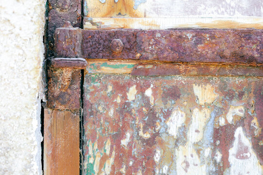 Close‑up of a rusted metal door hinge and peeling paint near Mandrakia, Milos, Greece, showing rich texture and color.