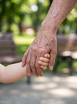 Elderly Grandparent Holding a Child's Hand Outdoors, Symbolizing Family Love and Intergenerational Bond