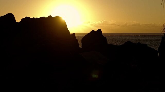 Aerial video along a tropical beach at dawn with golden sunrise over rocks