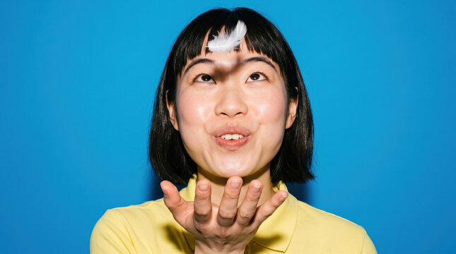 Person blowing a feather from their palm on a blue backdrop