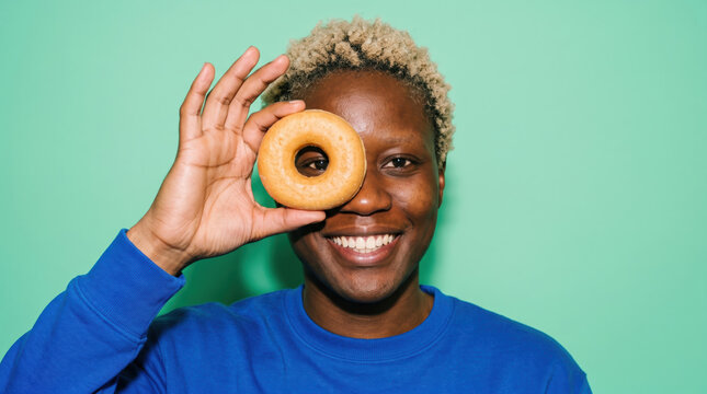 Smiling woman hold doughnut over eye on mint background