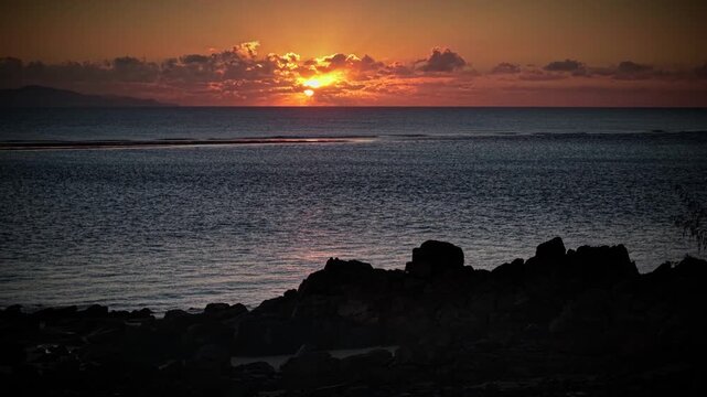 Aerial video along a tropical beach at dawn with golden sunrise over rocks