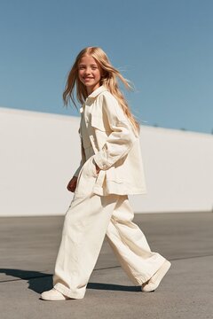 Modern children's fashion campaign shows a girl in an oversized cotton jacket and wide-leg trousers walking in a city Generative AI