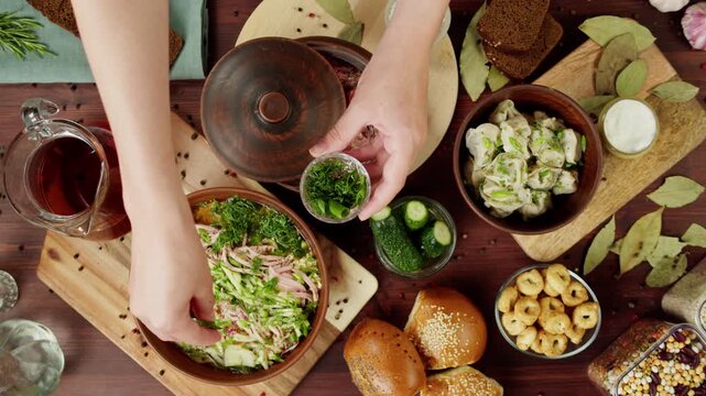 Traditional Slavic Cuisine. Pouring kvass into salad with greenery, cooking okroshka, summer cold soup. Ukrainian food, borsch in bowl. Dumplings and sour cream, fresh homemade pastry top view.