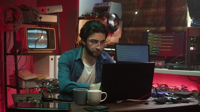 Hacker using laptop. Young Spanish man developing program in dark room. Professional programmer infecting system with cyber virus, typing on computer keyboard, breaking password.