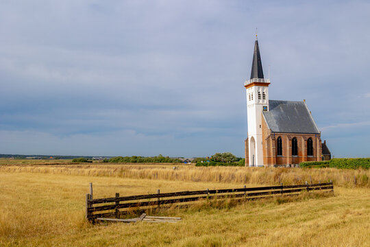 Typical landscape of Texel island with small village and picturesque church (Hervormde kerk) under blue sky and white clouds, A little town on the wadden islands, Den Hoorn, Noord Holland, Netherlands
