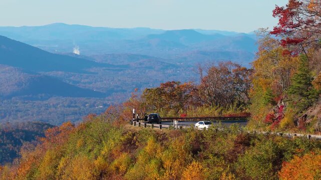 Peaceful scenic viewpoint featuring a parked car overlooking mountain fall foliage beneath clear skies in a tranquil natural setting.