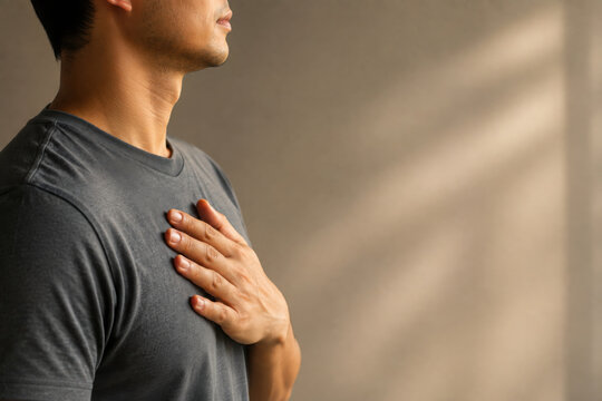 Man in gray shirt practices somatic healing by placing his hand on his chest feeling calm and peaceful in soft natural light