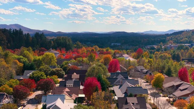Hillside homes surrounded by colorful woodland. Rolling mountain terrain creates beautiful residential landscape in autumn.