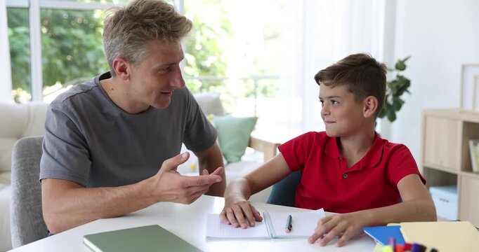 Father helping his son with homework at white table indoors