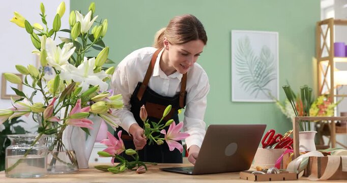 Florist using laptop while making bouquet of beautiful lilies at wooden table in shop
