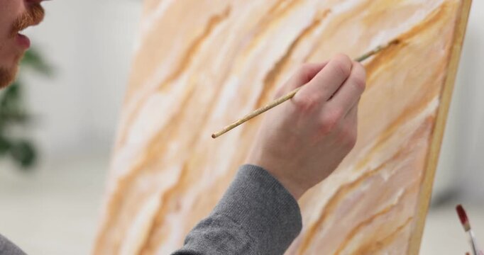 Man painting picture on easel in artist's studio, closeup. Camera moving up