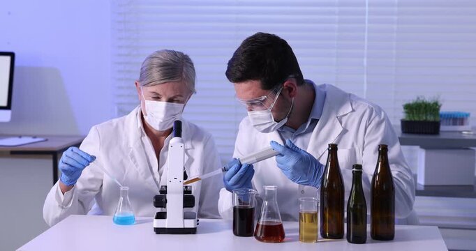 Quality control. Scientists in protective masks and gloves working with beer sample at white table in office
