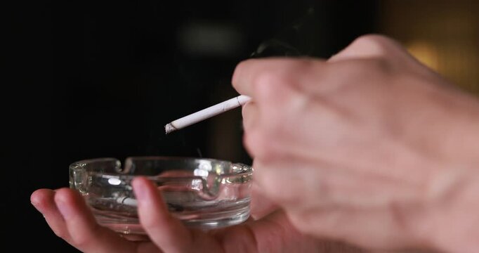 Man flicking ash from cigarette into ashtray indoors, closeup
