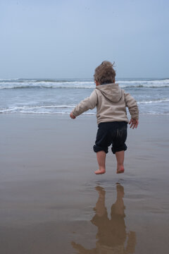 Toddler Boy Jumping Barefoot by the Sea on a Mild Winter Beach