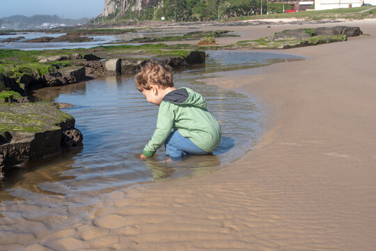 Two-Year-Old Toddler Boy Playing in Shallow Rocky Water at Prainha Beach, Torres, Brazil