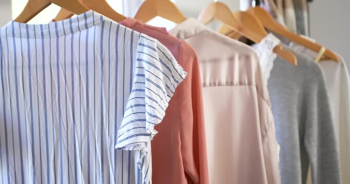Camera is pulling back and panning right to reveal garment row on wooden hangers near window