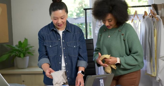 Smiling diverse female team opening cloth laying yellow flats in studio using tablet to plan