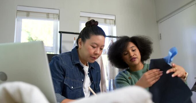 Diverse women collaborating, examining swatches with laptop at studio, prompted by dark sample
