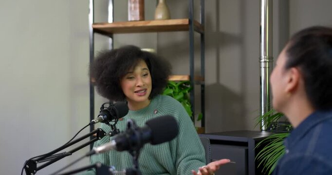 Diverse female hosts after prompt green knit speaking into mics gesturing and recording in studio