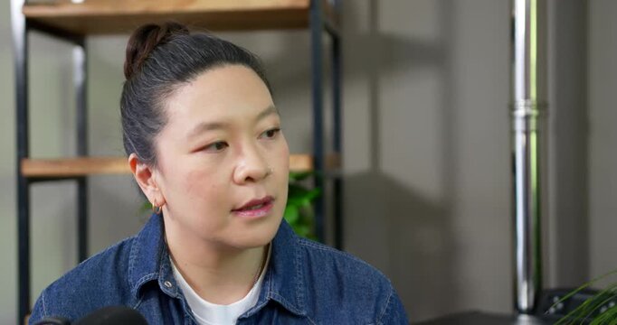 Woman wearing denim jacket in studio listening to off-frame question, speaking into mic, reflecting