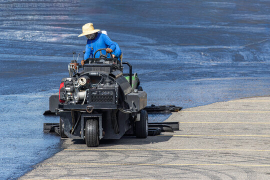 Road worker operating asphalt sealcoating machine applying fresh blacktop sealant on parking lot surface