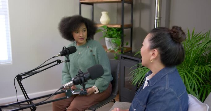 Asian and African American women recording, talking, gesturing with mics in studio interview