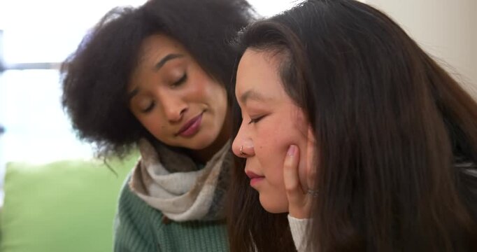 Diverse women on couch by window, Asian woman cupping cheek pensive, friend comforting, copy space