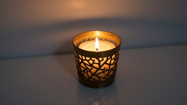 Decorative candle in an ornate metal holder with intricate cut-out pattern emitting warm light on a smooth surface