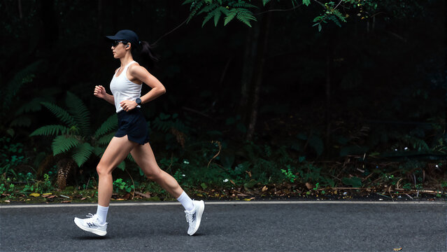 Side view of fit female runner sprinting along forest road in sportswear