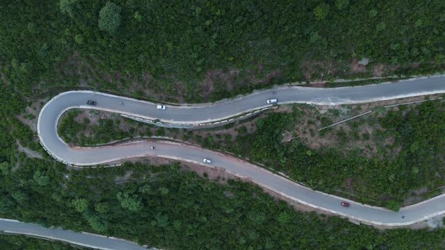Aerial top down of a sharp hairpin turn on a scenic mountain road, A curved forest highway showing active traffic and green hillside terrain